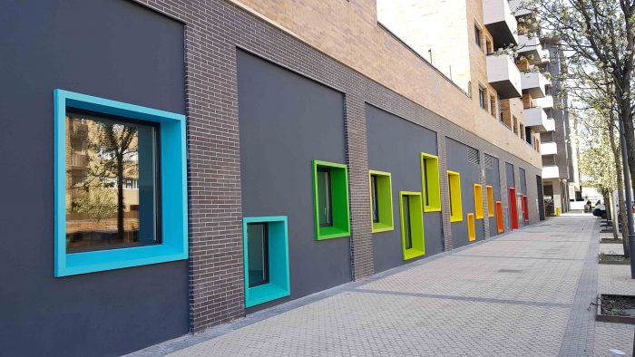 fachada de guarderia con ventanas cuadradas de distintas alturas y con su contorno en distintos colores