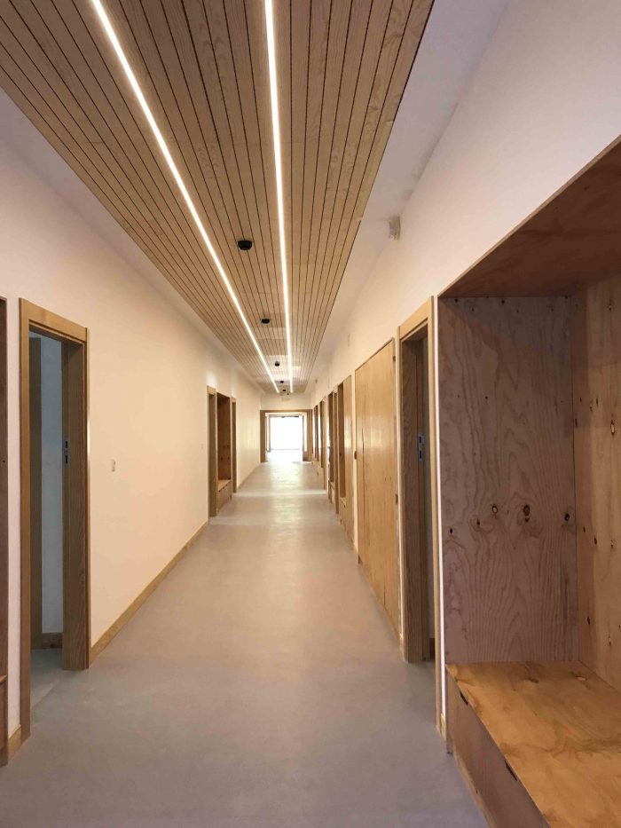 pasillo blanco con muebles de madera empotrados a ambos lados e iluminacion continua en el techo